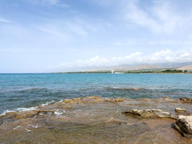Uçsuz bucaksız gökyüzünün altında Issyk-Kul 'un kayalık kıyısı ve berrak suyu.