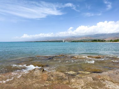 Uçsuz bucaksız gökyüzünün altında Issyk-Kul 'un kayalık kıyısı ve berrak suyu.