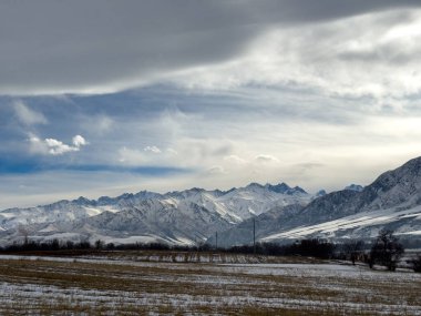 Kırgızistan 'da dağları kaplayan kar bulutlu kış gökyüzü altında huzurlu kırsal alan.