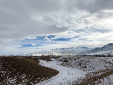Kırgızistan 'da dağları kaplayan kar bulutlu kış gökyüzü altında huzurlu kırsal alan.