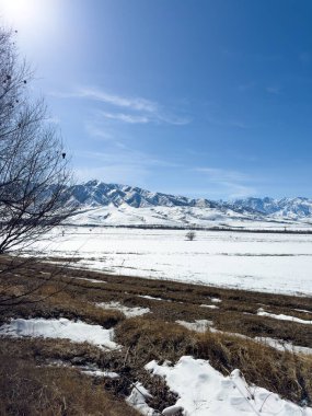 Kırgızistan 'da uzak sıradağları olan geniş karlı bir vadi. Parlak güneş ışığı ve derin mavi gökyüzü kış tarlaları üzerinde