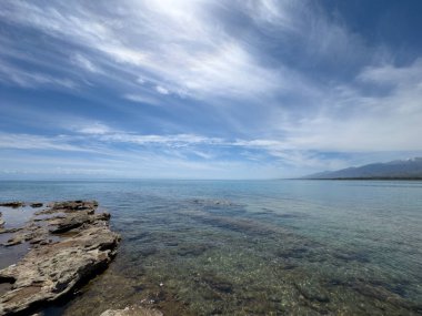 Uçsuz bucaksız gökyüzünün altında Issyk-Kul 'un kayalık kıyısı ve berrak suyu.