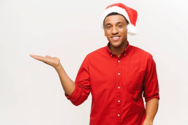 Kırmızı Noel Baba şapkalı mutlu Afro-Amerikalı adam elini boş fotokopi odasına uzatıyor. Genç adam dikkatinizi beyaza veriyor.
