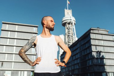 Şehir manzarasında dövmeli genç bir adamın portresi. Spor giyimli sporcu dışarıda antremana hazır, koşuya gidiyor.