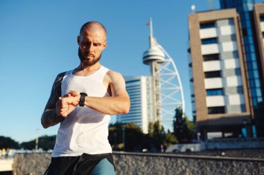 Yeni spor saatini koşu için kullanan dövmeli genç adam kalp atışlarını kontrol ediyor, modern teknolojiyi sağlıklı yaşam tarzı için kullanıyor.