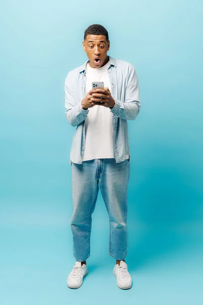 Εντυπωσιασμένος Μαθητής Casual Πουκάμισο Χρησιμοποιώντας Smartphone Απομονωμένο Μπλε Φόντο Σοκαρισμένος — Φωτογραφία Αρχείου