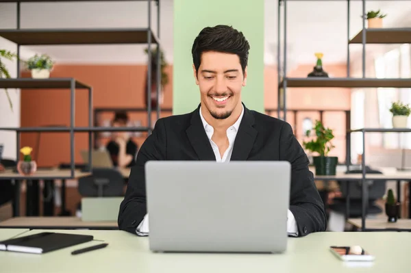 正式なスーツを着た正ラテン語の暗い髪のビジネスマンは ラップトップを使用して 現代のオフィススペースの机に座って ビジネス対応を行い 電子メールを返信します ヒスパニック系の男性オフィス従業員 — ストック写真