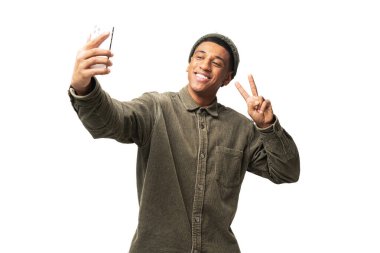 Waist up view of the young man showing victory gesture with his hand while chatting via cell phone or making selfie, isolated on white background