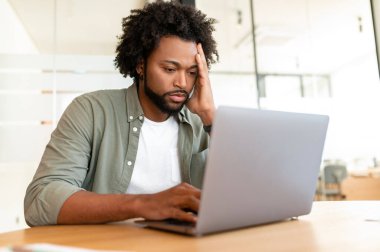 Fatigued businessman using laptop for working, the guy tired and burnout, holding head and feels headache, migraine sitting at the desk in modern office. Overwork and burnout concept