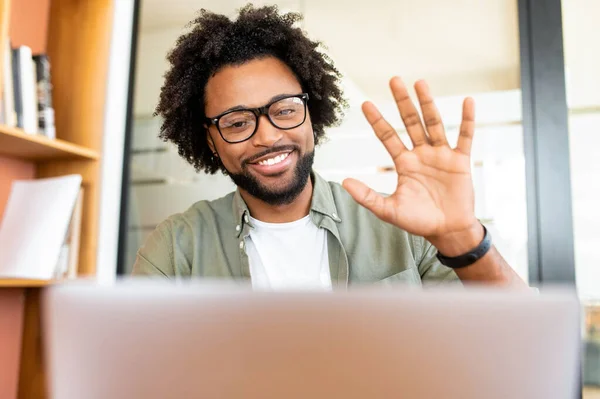 Glad to meet you. Happy joyful african-american guy making video call, man involved video conference, waving hand and greeting participants, studying on the distance, taking online class