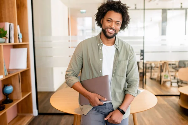 Smart and ambitious african-american male office employee posing with laptop indoor, friendly black business woman looking at the camera and smiles, beginner full of inspirations first day at work