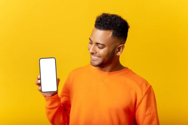 Handsome young man showing smartphone with blank screen and looking at screen, guy likes mobile app, feels satisfied, isolated