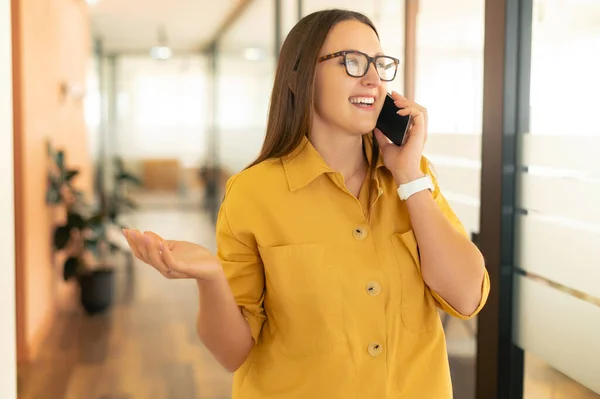 Happy cheerful female office employee talking on mobile phone and smiling, expressing positive emotions, young businesswoman is having a pleasant conversation in the office, baner