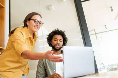 Teamwork. Close-up portrait of man and woman in smart casual clothes working in office with laptop. They are smiling and discussing some issues