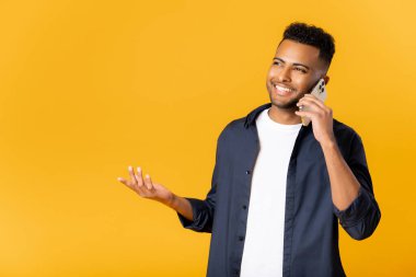 Mobile communication. Portrait of indian man making call to consult, having pleasure talk on cellphone, discussing great news. Indoor studio shot isolated on yellow background