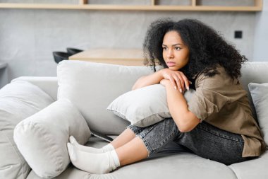 Üzgün kadın kanepede oturuyor, pencereden bakıyor, gelecek için endişeli ve stresli hissediyor ve kendi sorunlarını düşünüyor.