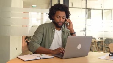 Kendine güvenen Afro-Amerikalı iş adamı telefonda bazı notlar yazıyor ofiste oturuyor, arkadaş canlısı erkek çalışanlar müşterilerle cep telefonuyla konuşuyor, bilgisayarın önünde akıllı telefondan sohbet ediyor.