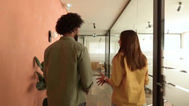 The camera follows two friendly colleagues walking through hallway in modern office. Young business people are talking, discussing and gesturing, manager explains something to colleague