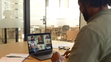 View from back above shoulder on the laptop with diverse employees, coworkers on the screen, video call, online meeting. African guy using app for video conference with many people together