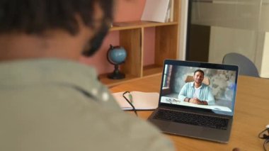 African-American man with curly hair using app for distance video communication with Indian coworker, friend, meeting online, looking and waving at laptop desktop with male profile, studying online