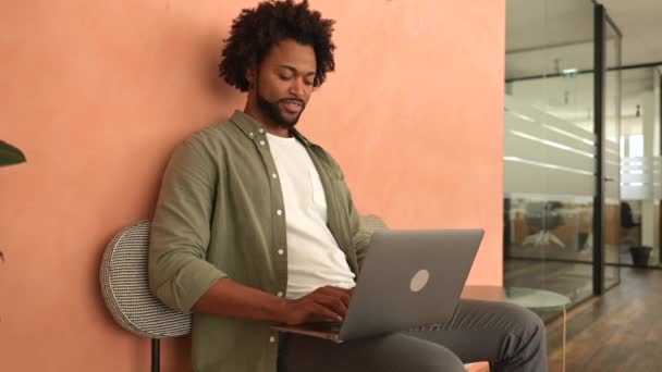 Positiver Junger Afrikanisch Amerikanischer Mann Der Büro Loft Stil Sitzt — Stockvideo