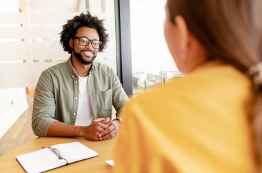 Two colleagues discussion project sitting together in the coworking space, man and woman looking at each other and solving tasks in relaxed office atmosphere, talking in order to reach a decision