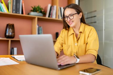 Gözlüklü genç bir kadının portresi masada dizüstü bilgisayarla oturuyor, bir e-posta yazıyor, iş arkadaşlarıyla mesajlaşıyor, sohbet ediyor, hoş bir gülümsemeyle iş anlarını tartışıyor.