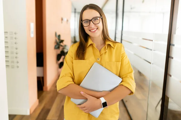 Gözlüklü Gülümseyen Bir Kadın Kameraya Bakıyor Ofis Koridorunda Duruyor Dizüstü — Stok fotoğraf