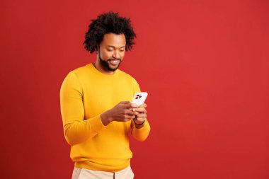 Sakallı çekici bir adamın portresi mutlu bir ifadeyle cep telefonu kullanıyor, akıllı telefona bağımlı, sosyal ağda mesajlaşıyor. Kırmızı arkaplanda kapalı stüdyo çekimleri