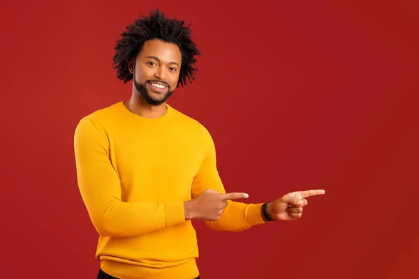 陽気なアフリカ系アメリカ人の男は 赤い背景に隔離された空のコピースペースで指を指します 多人種男性は取引をお勧めします あなたの注意を払います 新製品を提示 — ストック写真