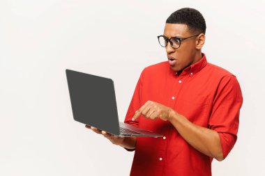 Şok olmuş genç Afrikalı Amerikalı adam elinde dizüstü bilgisayarla beyaz duvarda duruyor ve mesaj yazıyor, sohbet ediyor, yeni bir uygulama kullanıyor, korkutma düğmesine basıyor.