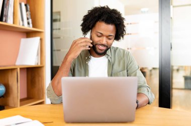 Erkek ofis çalışanı müşterilerle yazışıyor ve bağlantı kuruyor. Akıllı gündelik giyinen, kendine güveni tam Afro-Amerikan bir adam. Laptop kullanıyor ve iş yerinde otururken akıllı telefondan konuşuyor.