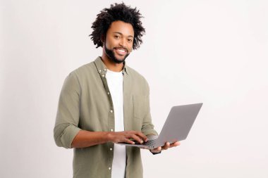 Elinde dizüstü bilgisayarla gülümseyen ve yazan olumlu bir adam. Blogcu sosyal ağlarda yazılar yazıyor, takipçilerle sohbet ediyor. Beyaz arka planda izole edilmiş kapalı stüdyo görüntüleri