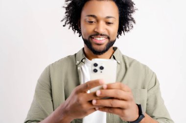 Neşeli genç siyahi adamın portresi beyaz arka planda cep telefonundan mesaj yolluyor. Akıllı telefon kullanan, internette sohbet eden, sosyal ağlarda mesajlaşan mutlu Afro-Amerikalı adam.