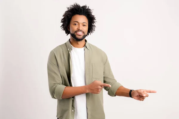 stock image Pleasant looking curly man pointing finger aside at copy space, showing area for advertisement. Indoor studio shot isolated on white background