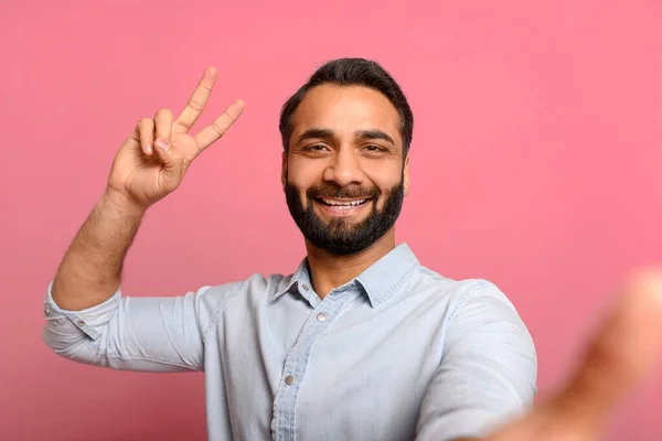 快乐的印度年轻人正在用智能手机进行视频通话 微笑的男人在网上交流 记录博客 享受与粉色人群隔离的在线对话 把V字显示在相机上 — 图库照片