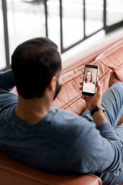 Hintli bir adamın mobil flört uygulaması kullanarak dinlendiği dikey bir fotoğraf, video bağlantısı üzerinden bir kadınla konuşmak, koyu renk saçlı Latin bir adamın kadınlara video konuşması.