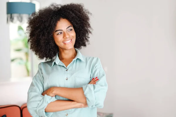 Smiling Curly Woman Standing Modern Apartment Looking Aside Dreamly Young — Stock Photo, Image