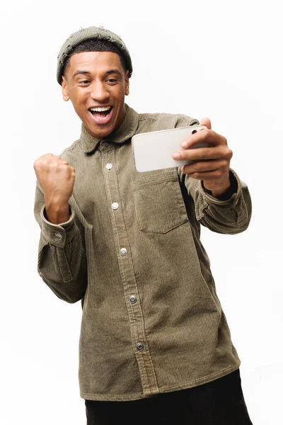 stock image Excited young man playing video game on the smartphone isolated on white background, hispanic gambling guy spends leisure time with video games, celebrating victory, creaming yes