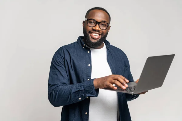 Usmívající Africký Muž Používající Notebook Stojící Šedém Pozadí Kontrolující Domácí — Stock fotografie