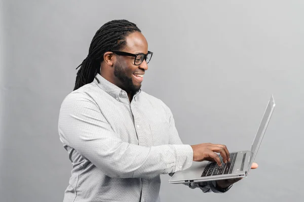 Ung Afroamerikansk Man Står Isolerad Grå Vägg Håller Bärbar Dator — Stockfoto