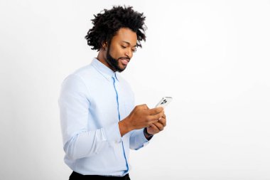 Kıvırcık saçlı, cep telefonu kullanan, mesaj yazan ya da haberciyle sohbet eden Afro-Amerikan bir adamın yan görüntüsü. Teknoloji konsepti. Beyaz arka planda izole edilmiş kapalı stüdyo görüntüleri