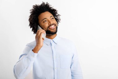 Kıvırcık, güler yüzlü beyaz gömlekli mutlu Afro-Amerikan adam cep telefonuyla konuşuyor, beyaz arka planda izole edilmiş hoş bir sohbet yürütüyor, stüdyo portresi.