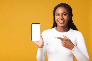 Sarı arka planda tek başına duran ve reklam için akıllı telefonu işaret eden mutlu çok ırklı kadın. Teknoloji ve insanlar kavramı