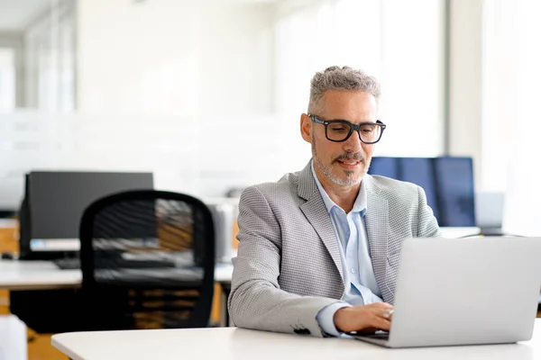 穿着智能休闲装的中年商人坐在现代化的办公室里 头戴灰色头发的高级自由职业者在网络上打字 发短信 研究和探索信息 — 图库照片