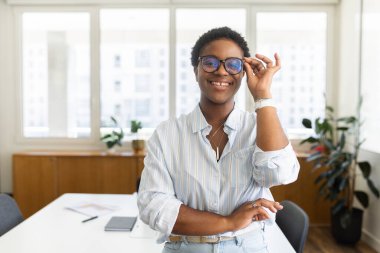 Çekici karizmatik Afro-Amerikalı genç iş kadını modaya uygun gözlük takıyor gülümsüyor ve kameraya bakıyor, bayan ofis çalışanı, yönetici, kısa saç kesimi ayarlayan gözlüklü CEO.