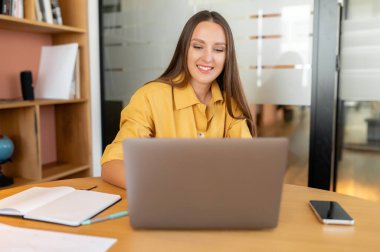 Akıllı ve hırslı bir ofis çalışanı dizüstü bilgisayar kullanıyor. Dost canlısı bir iş kadını ekrana bakıyor ve gülümsüyor.