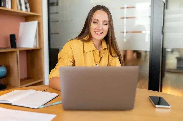スマートで野心的な女性オフィスの従業員は ラップトップコンピュータを使用しています スクリーンと笑顔を見ているフレンドリーなビジネス女性 仕事で初日 — ストック写真