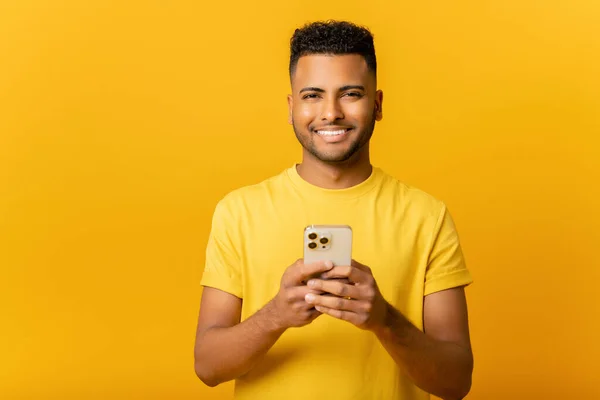 一个开朗的印度小伙子用黄色背景的手机传递信息的画像 快乐的阿拉伯人使用智能手机 喜欢网上聊天 在社交网络上发短信 — 图库照片
