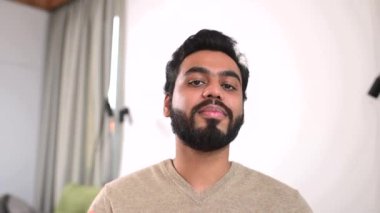 Masada oturan ve el kol hareketi yapan mutlu Hintli genç adamın portresi. Gülümseyen etnik adam sanal bir buluşmaya dahil oldu. Latin erkek öğrenci eğitim konferansına katılıyor.